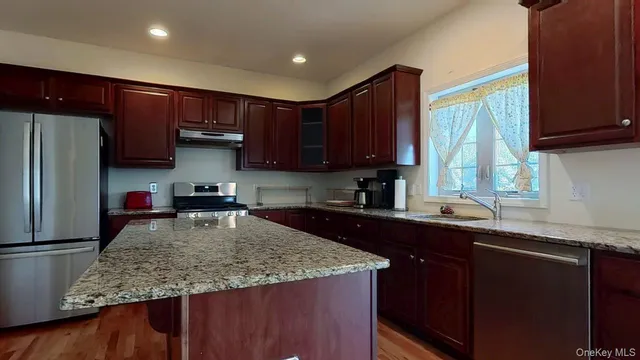 a large kitchen with stainless steel appliances granite countertop a stove top oven a sink dishwasher and a refrigerator with wooden floor