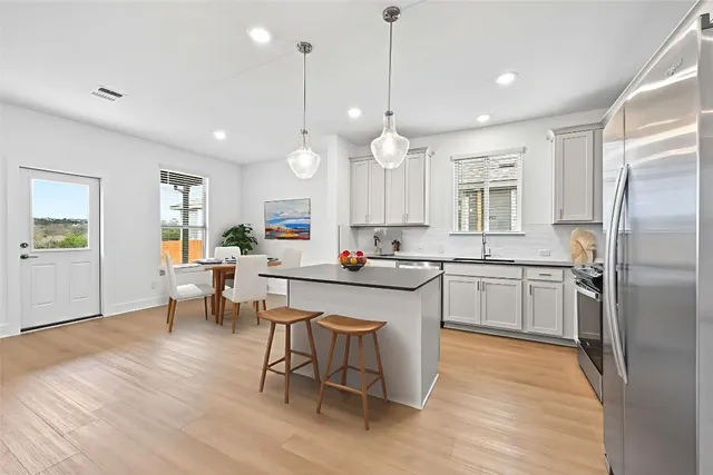 a open kitchen with stainless steel appliances granite countertop a refrigerator a sink dishwasher a dining table and chairs with wooden floor