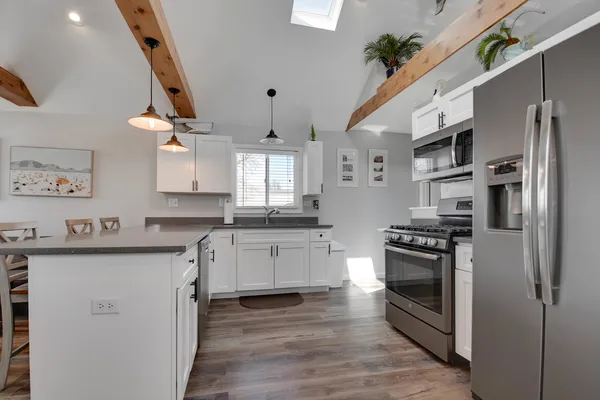 a kitchen with stainless steel appliances a stove a sink dishwasher a refrigerator white cabinets and wooden floor