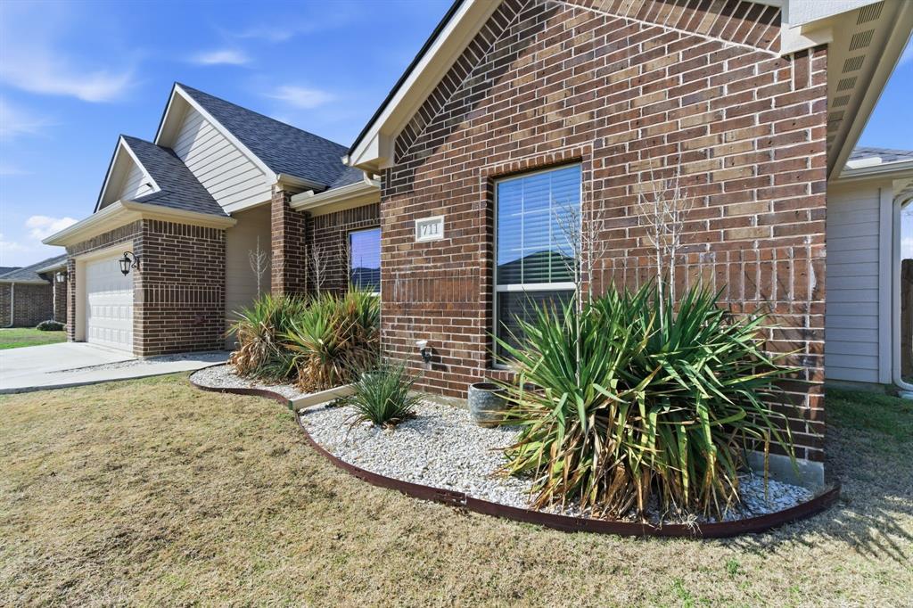 711 Hadley Lane Valley View, TX 76272 - Photo 32 of 40 View of home's exterior with brick siding, an attached garage, a yard, roof with shingles, and concrete driveway