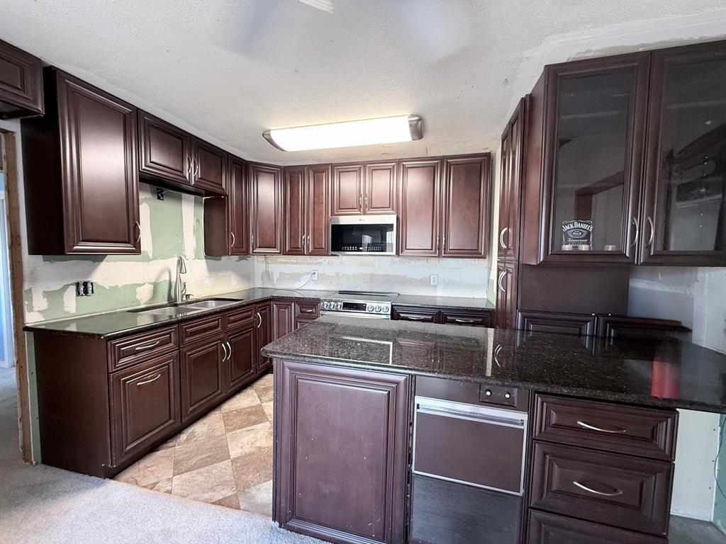 312 Ralph Street White Settlement, TX 76108 - Photo 21 of 32 Dark wood-finish cabinetry with silver hardware, dark countertops, built-in stainless steel microwave, and a stainless steel oven