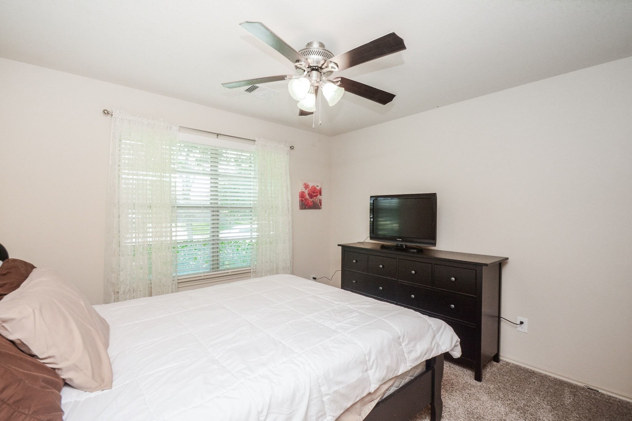 23318 Dukes Run Drive Spring, TX 77373 - Photo 20 of 41 Cozy bedroom with neutral walls and carpet, featuring a ceiling fan and a large window for natural light. Includes space for a comfortable bed and a dresser with room to spare.