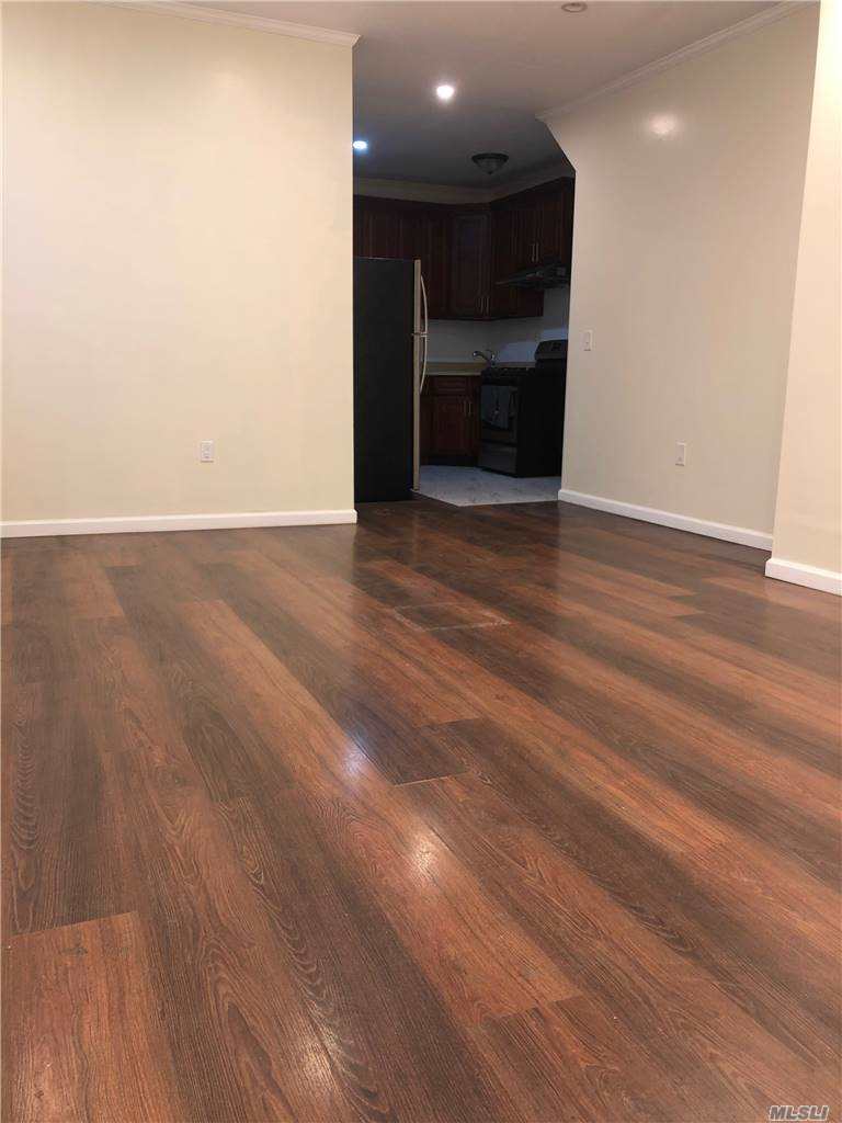 an empty room with wooden floor and kitchen