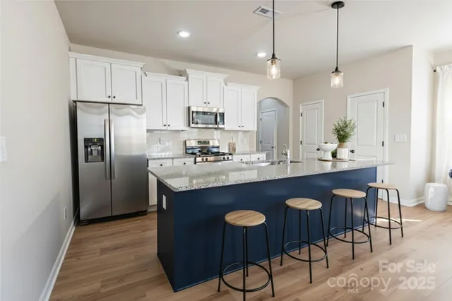 a kitchen with stainless steel appliances granite countertop a sink a stove a refrigerator and island with wooden floor