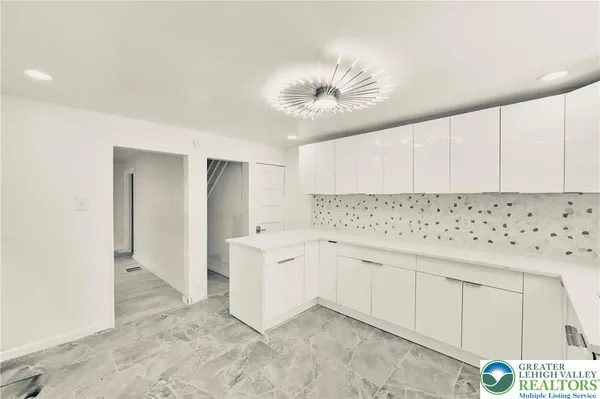 a room with a chandelier fan and kitchen view