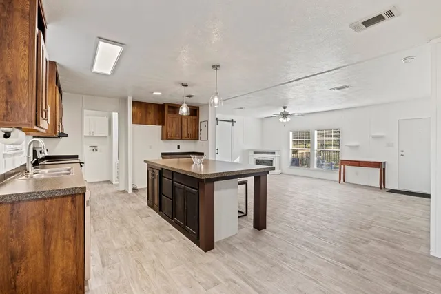 a kitchen with stainless steel appliances granite countertop a stove top oven a sink dishwasher a refrigerator and a dining table with wooden floor
