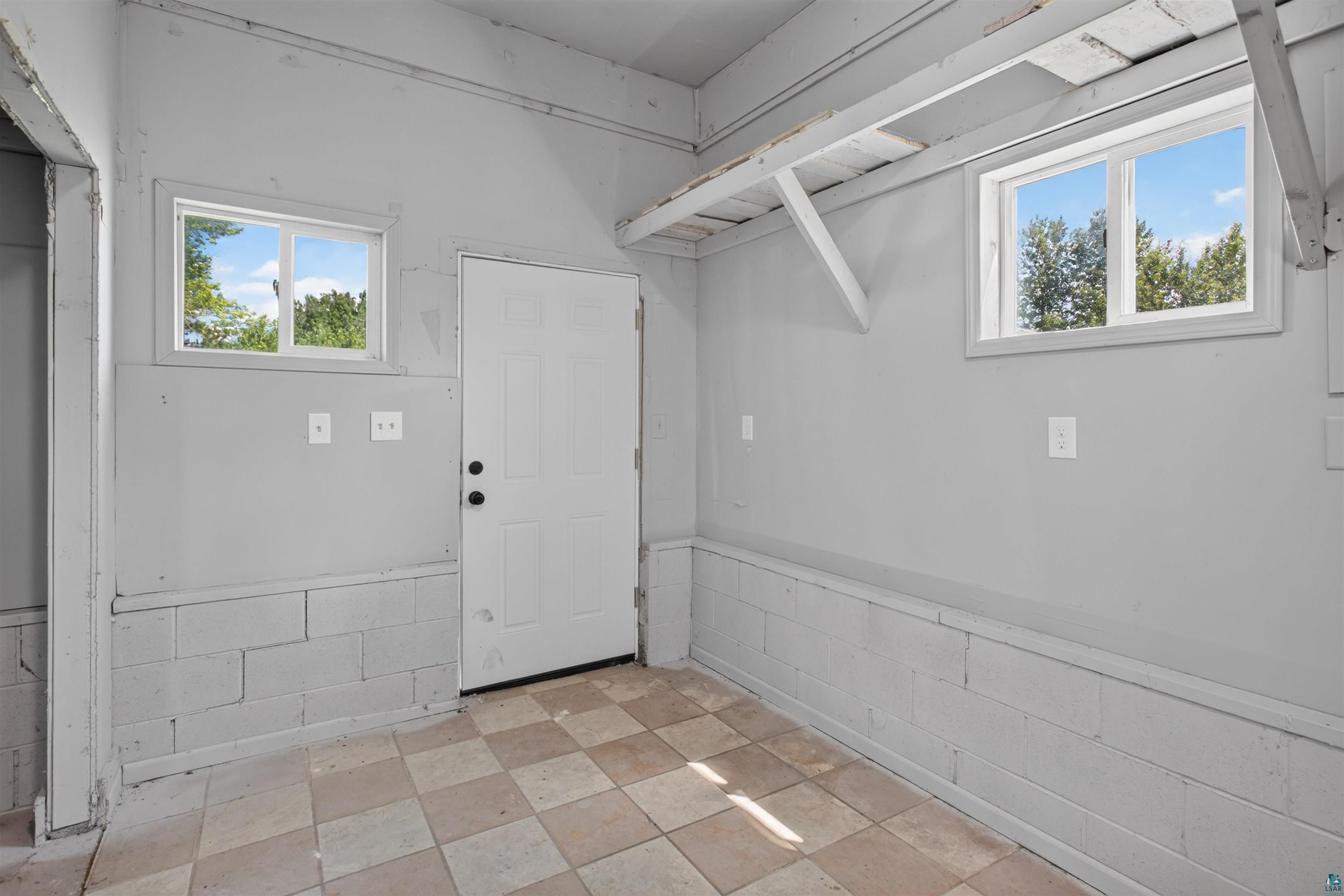 5868 Rice Lake Road Duluth, MN 55803 - Photo 33 of 39 Utility space featuring a checkered tile floor, two windows providing natural light, a white paneled door, and exposed rafters