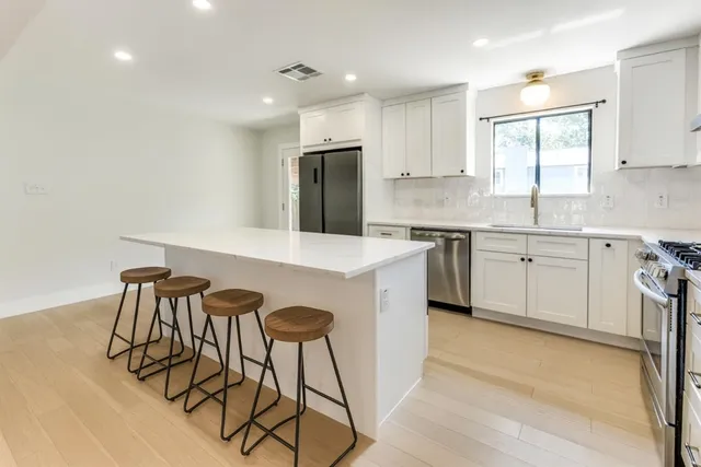 a kitchen with stainless steel appliances granite countertop a sink a stove a refrigerator and island with wooden floor