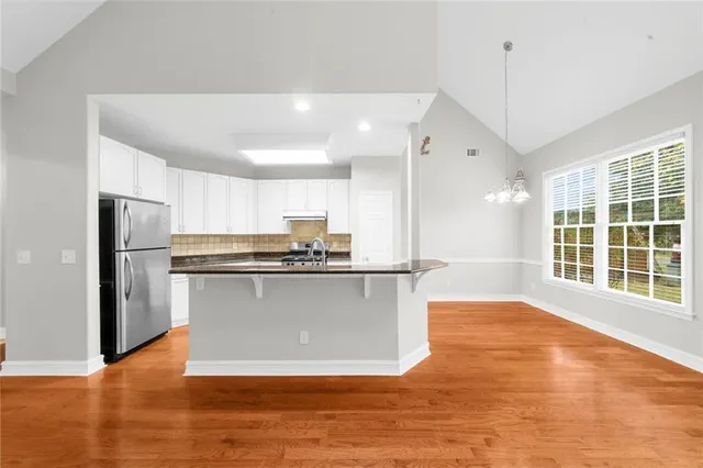 a view of a kitchen with stainless steel appliances granite countertop a refrigerator a sink dishwasher a oven with white cabinets and wooden floor