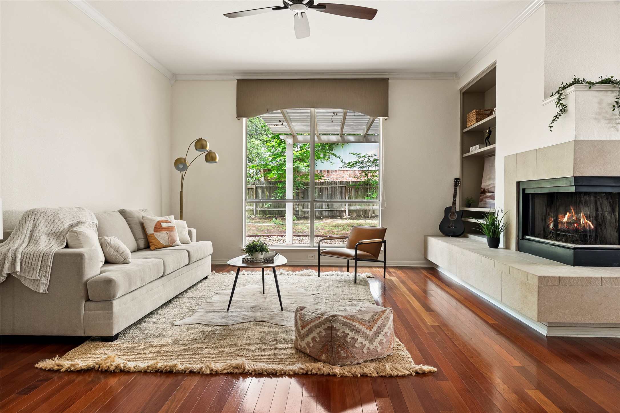 Living room featuring dark wood-style flooring, built in features, a tile fireplace, ornamental molding, and a ceiling fan