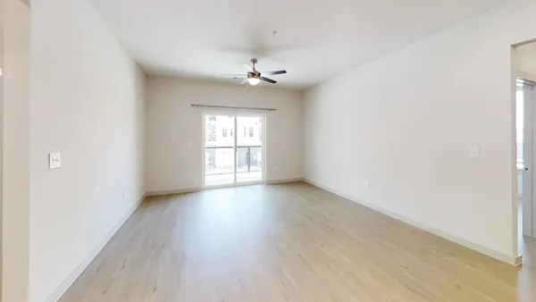 an empty room with wooden floor chandelier fan and windows