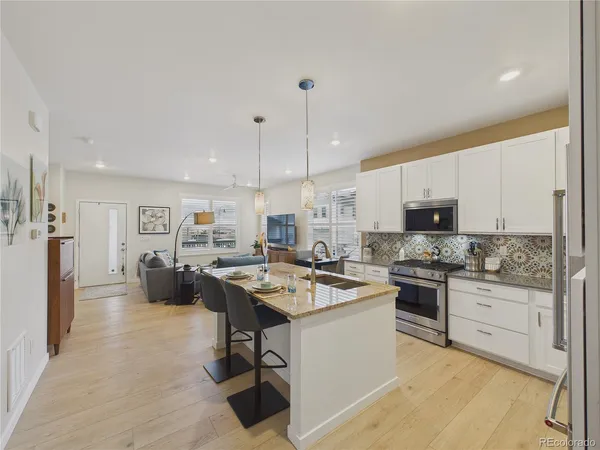 a kitchen with stainless steel appliances kitchen island granite countertop a stove a sink a refrigerator and white cabinets with wooden floor