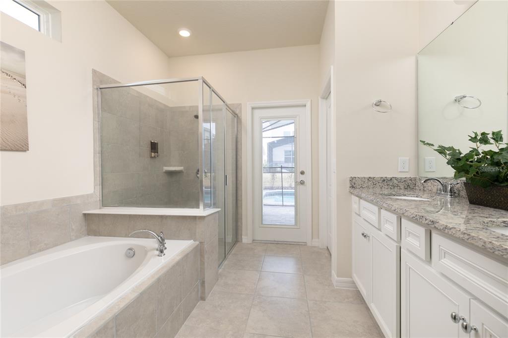 7208 Oakmoss Loop Davenport, FL 33837 - Photo 19 of 46 a spacious bathroom with a granite countertop tub a double vanity sink and mirror