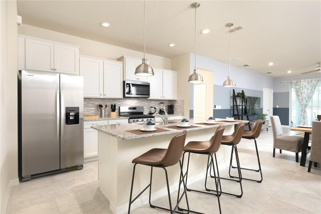 7208 Oakmoss Loop Davenport, FL 33837 - Photo 5 of 46 a kitchen with stainless steel appliances kitchen island granite countertop a refrigerator and a stove top oven