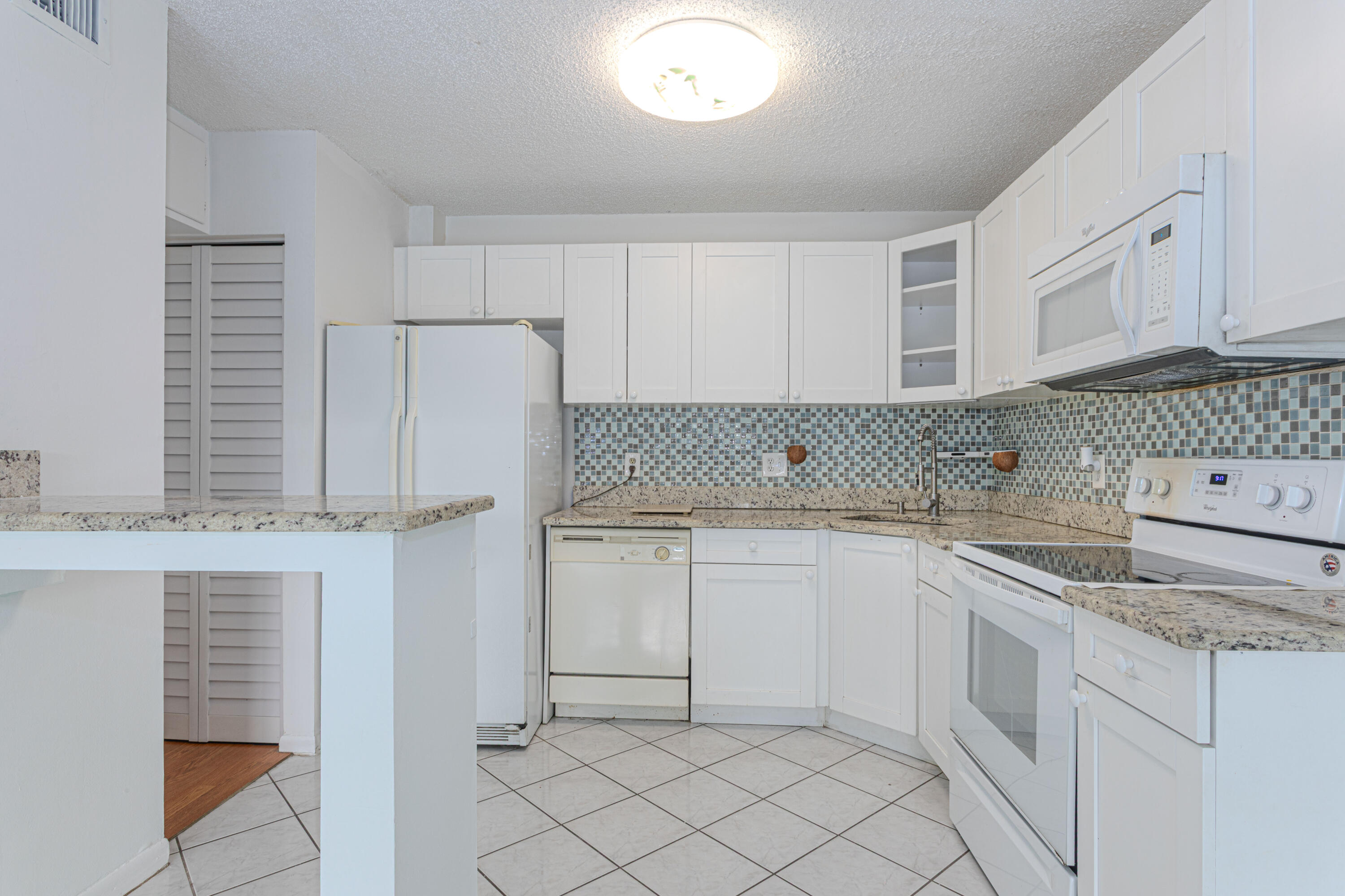603 Sea Pine Way, Unit C1 Greenacres, FL 33415 - Photo 9 of 32 a kitchen with granite countertop white cabinets and white appliances