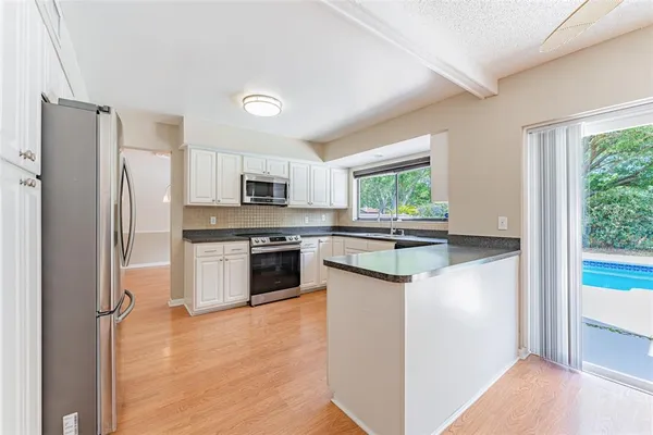 a kitchen with stainless steel appliances kitchen island granite countertop a refrigerator a stove a oven with white cabinets and wooden floor