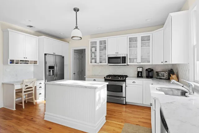 a kitchen with stainless steel appliances granite countertop a stove top oven a refrigerator a sink and white cabinets with wooden floor