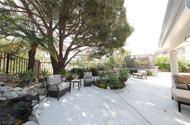 a view of a patio with couches and table and chairs under an umbrella with large trees