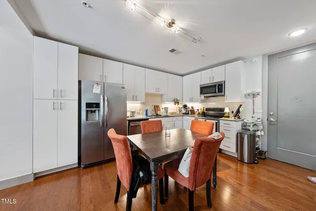 a kitchen with stainless steel appliances a dining table chairs refrigerator and microwave