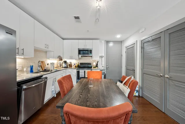 a kitchen with stainless steel appliances granite countertop a sink dishwasher a stove a refrigerator with a dining table and chairs