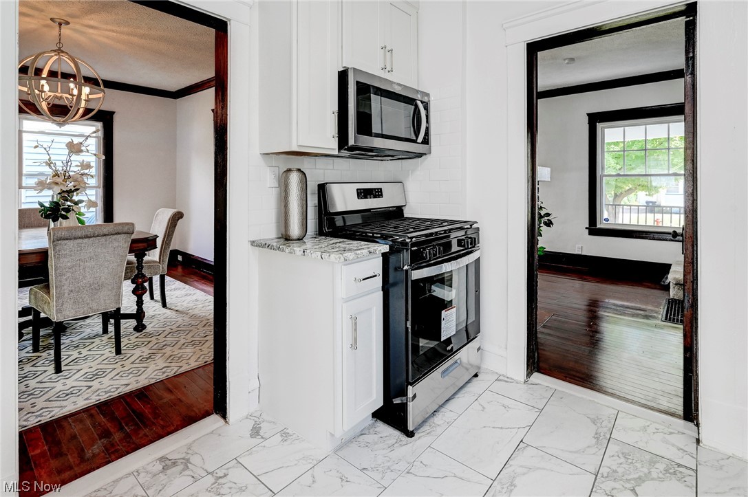 4464 Broadale Road Cleveland, OH 44109 - Photo 11 of 26 Kitchen with appliances with stainless steel finishes, white cabinets, ornamental molding, backsplash, and light tile floors