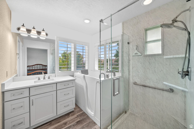 1464 990 West Provo, UT 84601 - Photo 21 of 41 Spacious bathroom featuring a walk-in tub, separate glass-enclosed shower, dual-sink vanity with a quartz countertop, and wood-finish flooring