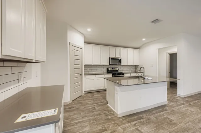 a kitchen with stainless steel appliances granite countertop a stove top oven a sink a refrigerator and white cabinets