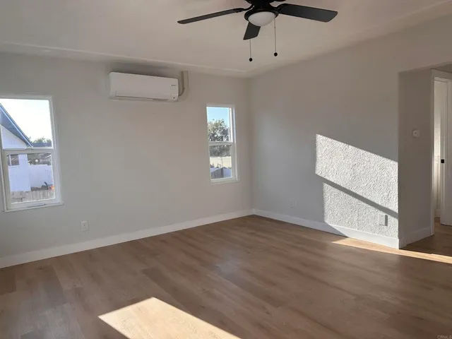 an empty room with wooden floor ceiling fan and windows