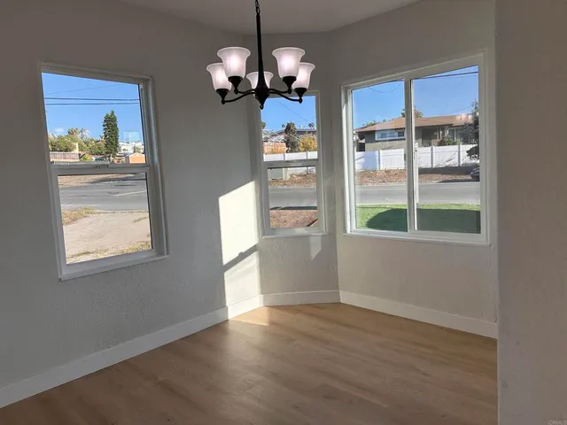 a view of a room with wooden floor a chandelier and windows