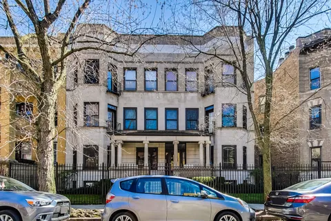 a front view of a building with lot of cars and trees