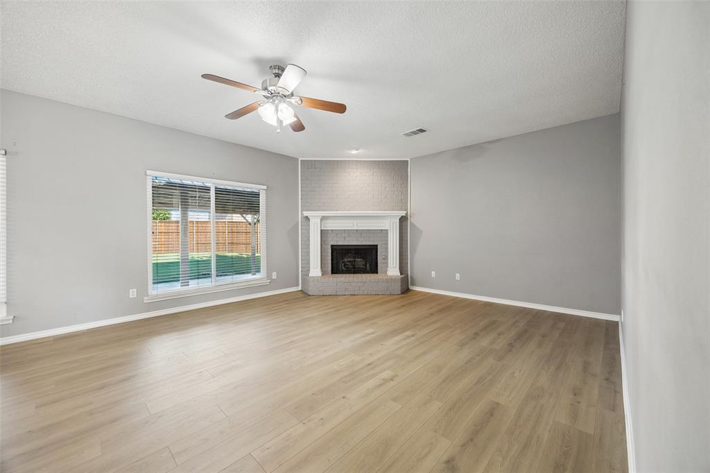 753 Summerfield Drive Allen, TX 75002 - Photo 9 of 40 Spacious room featuring wood-finish flooring, light gray walls, a ceiling fan with integrated lighting, and a brick fireplace with a white mantel