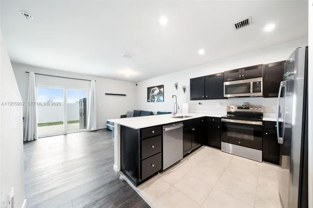 a large kitchen with stainless steel appliances kitchen island granite countertop a refrigerator a stove top oven a sink with wooden cabinets and wooden floor