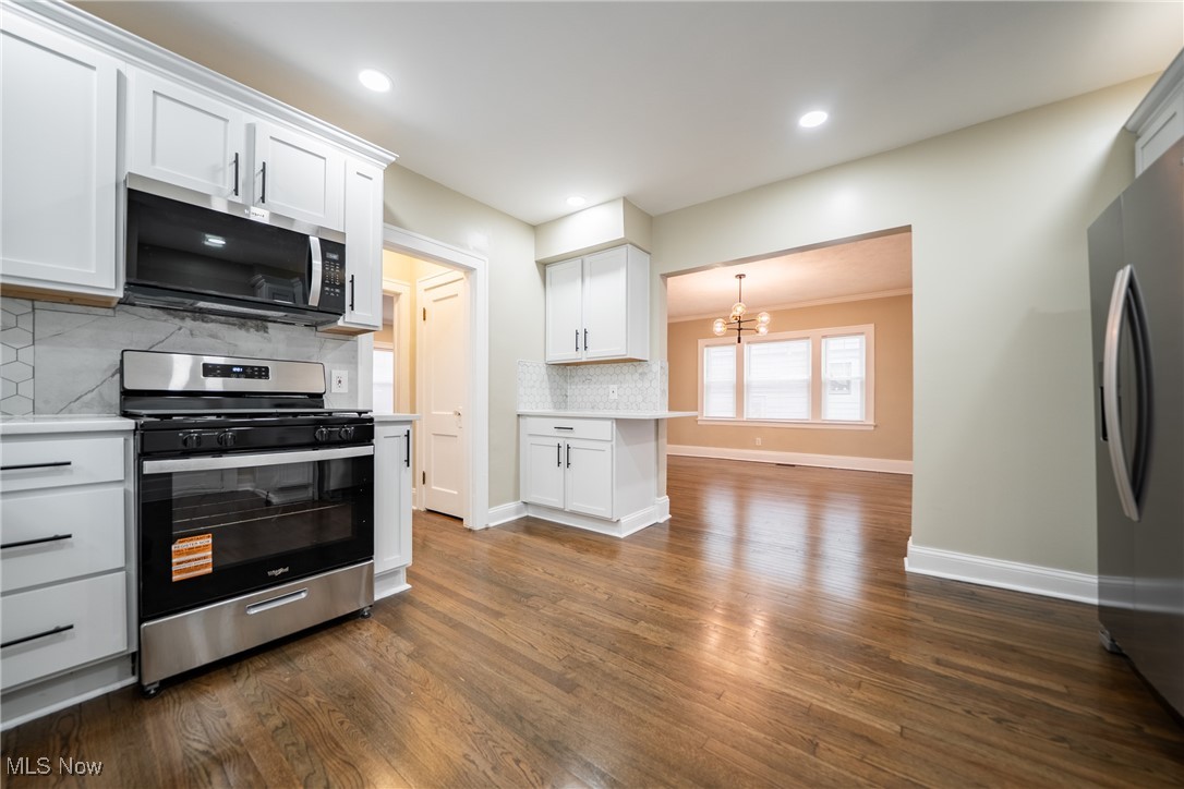 3816 Summit Park Road Cleveland Heights, OH 44121 - Photo 12 of 35 Kitchen with appliances with stainless steel finishes, white cabinets, a chandelier, backsplash, and dark wood-style flooring