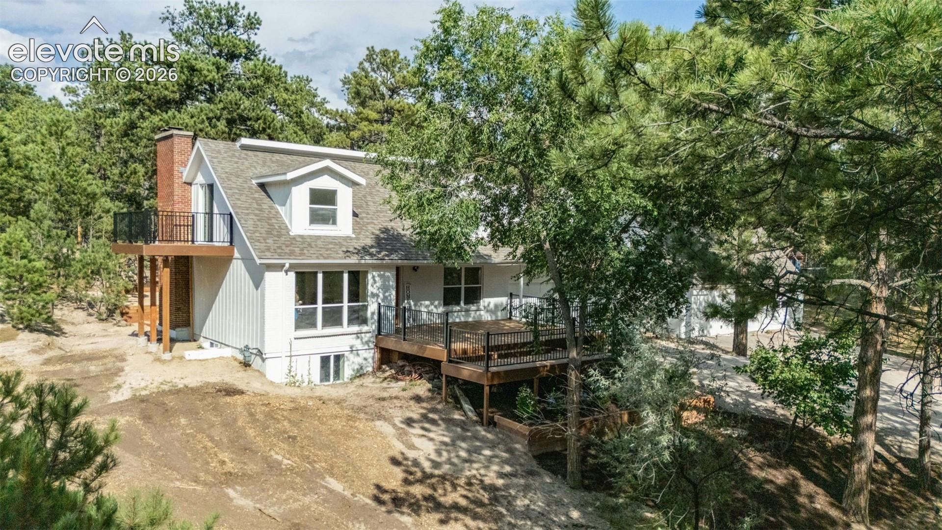 Back of property with a shingled roof, a chimney, a deck, and a balcony