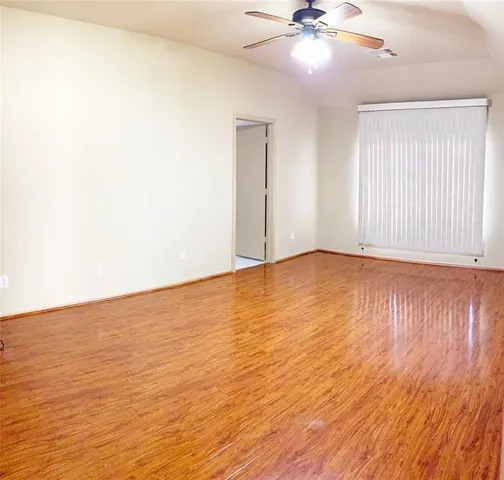 an empty room with wooden floor chandelier fan and windows