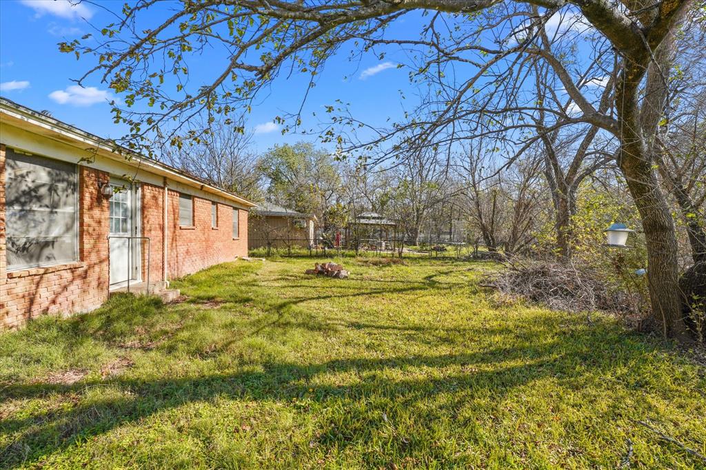 12924 Mitchell Drive Balch Springs, TX 75180 - Photo 14 of 14 a backyard of a house with large trees and a wooden fence