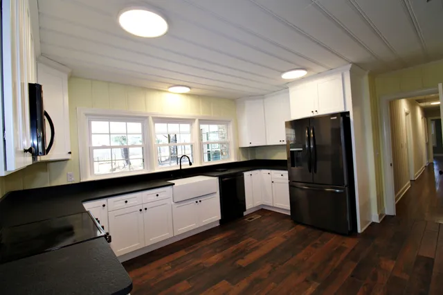 a kitchen with granite countertop a refrigerator a sink dishwasher a stove and white countertops with wooden floor