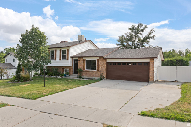 Split-level home featuring a two-car garage with a brown door, white siding, and brick accents