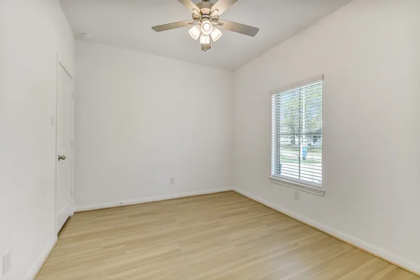 an empty room with wooden floor chandelier fan and windows