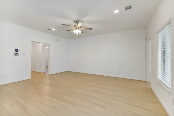 an empty room with wooden floor chandelier fan and windows