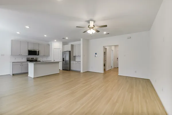 a view of an empty room and kitchen with wooden floor