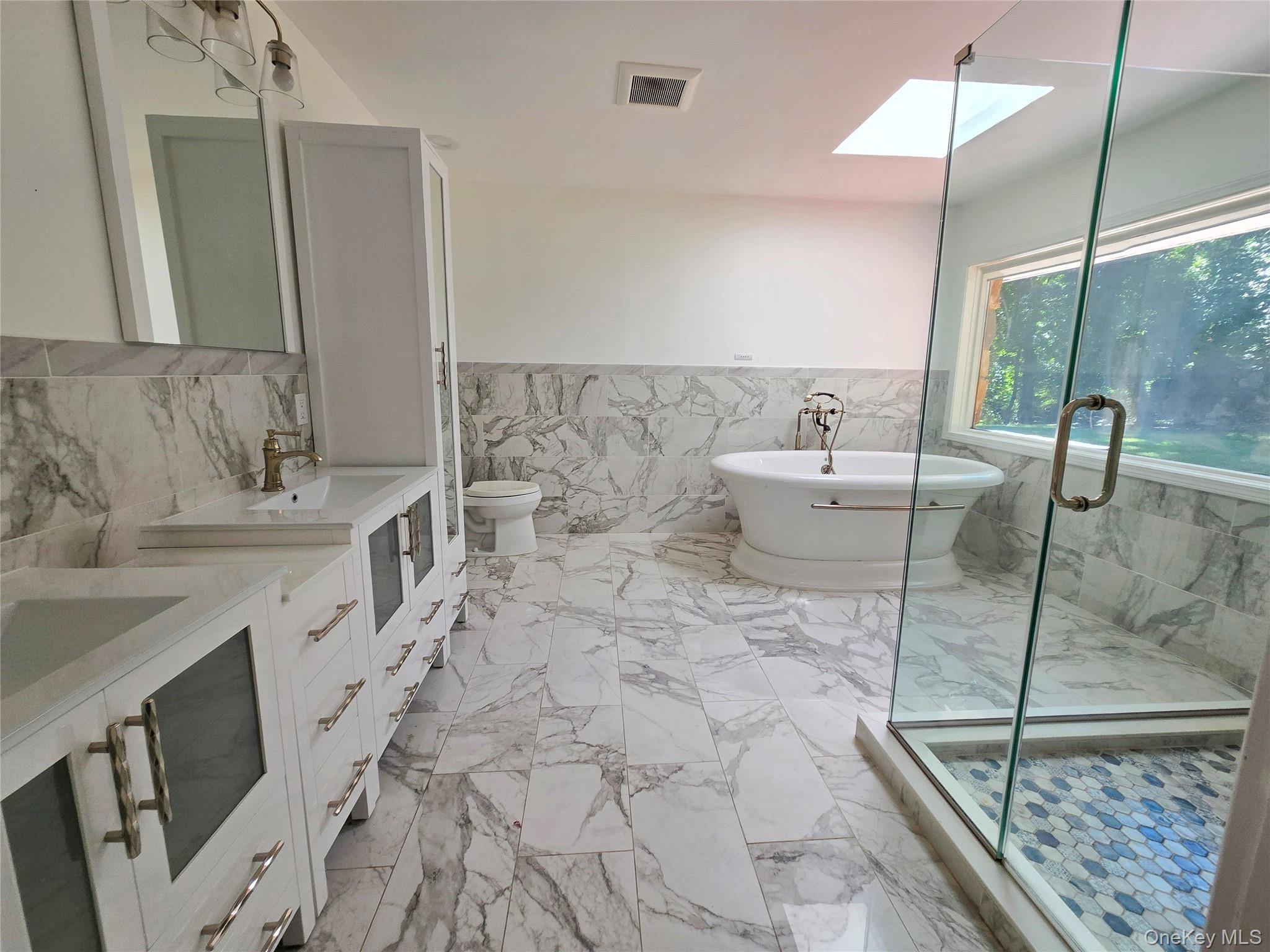 32 Valley Road Old Westbury, NY 11568 - Photo 40 of 45 Bathroom featuring tile walls, wainscoting, a skylight, double vanity, and a freestanding tub