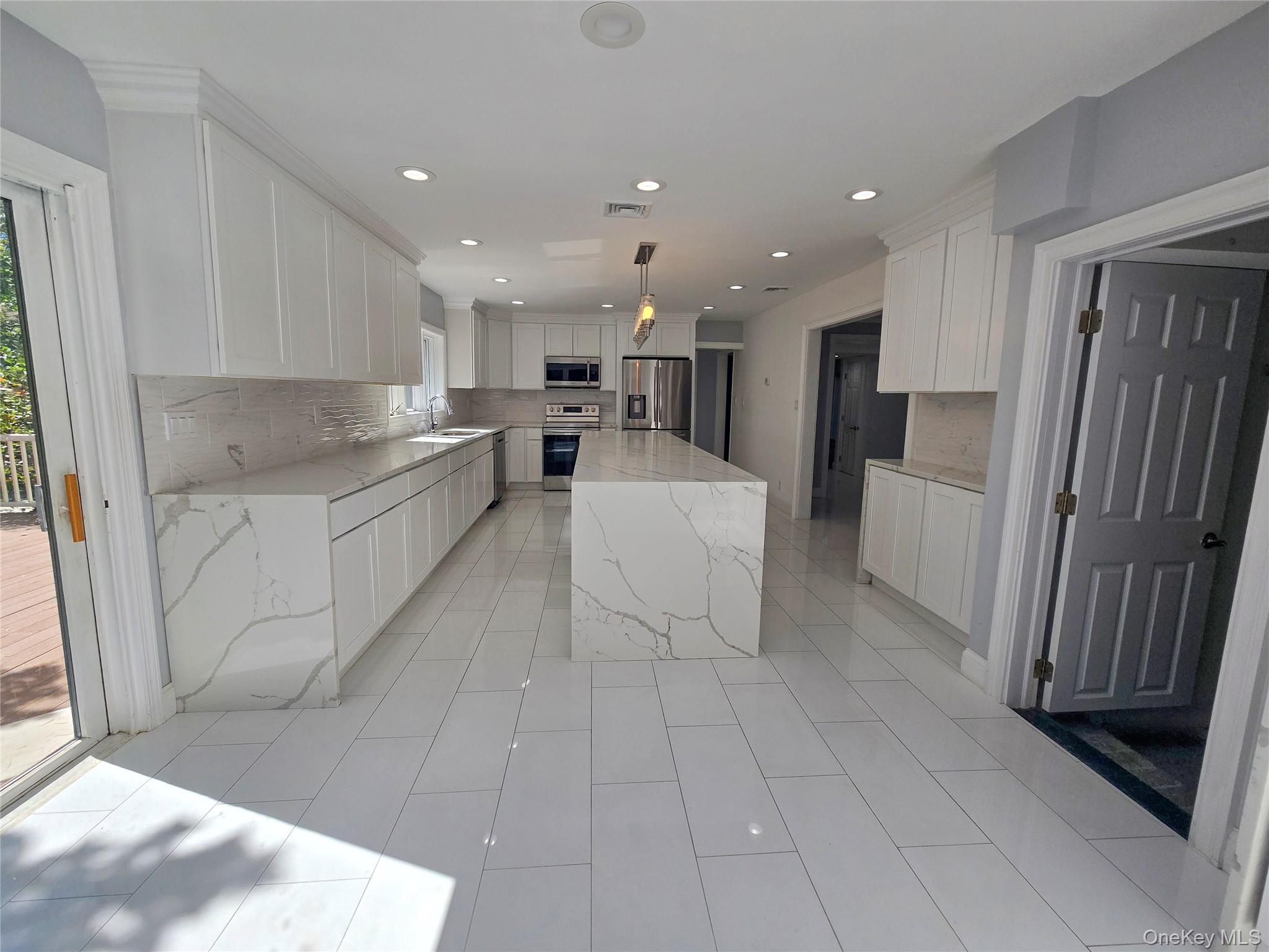 32 Valley Road Old Westbury, NY 11568 - Photo 45 of 45 Kitchen featuring tasteful backsplash, white cabinets, light stone counters, hanging light fixtures, and stainless steel appliances