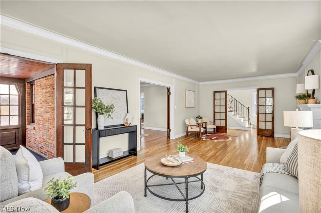 3145 Huntington Road Shaker Heights, OH 44120 - Photo 7 of 28 Spacious living room featuring hardwood flooring, crown molding, a brick sunroom with wood-paneled ceiling, and French doors opening to an entryway with a staircase