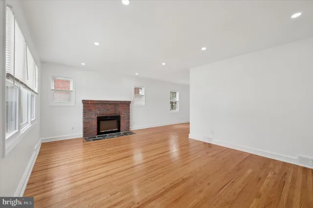 a view of an empty room with wooden floor fireplace and a window