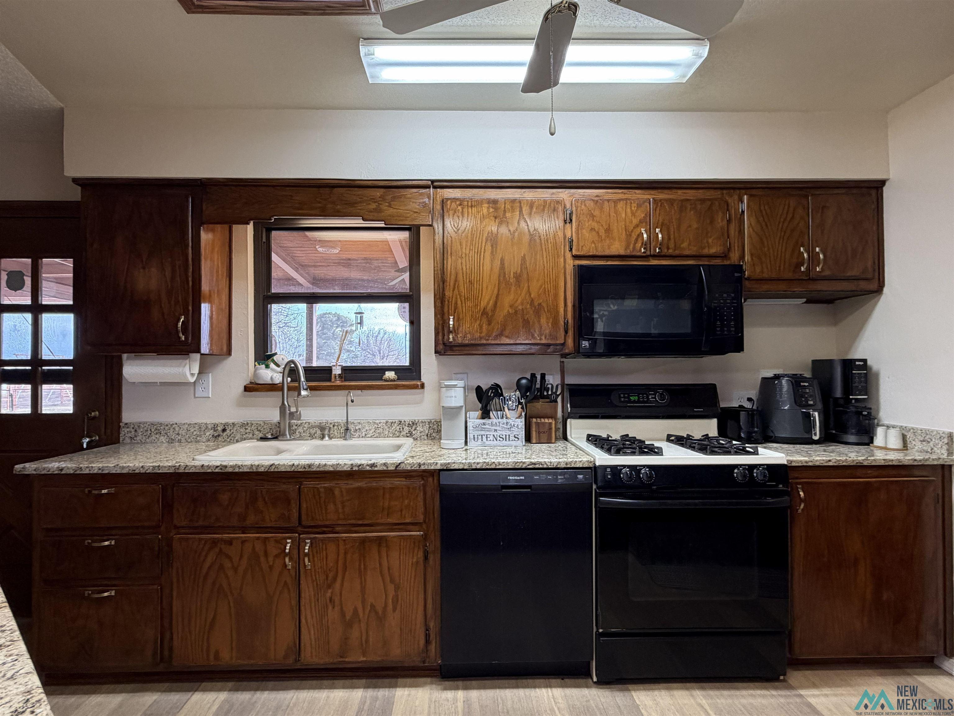 2001 East Derrick Road Carlsbad, NM 88220 - Photo 49 of 84 Kitchen with black appliances, ceiling fan, dark wood finish cabinets, light stone countertops, and light wood-style floors