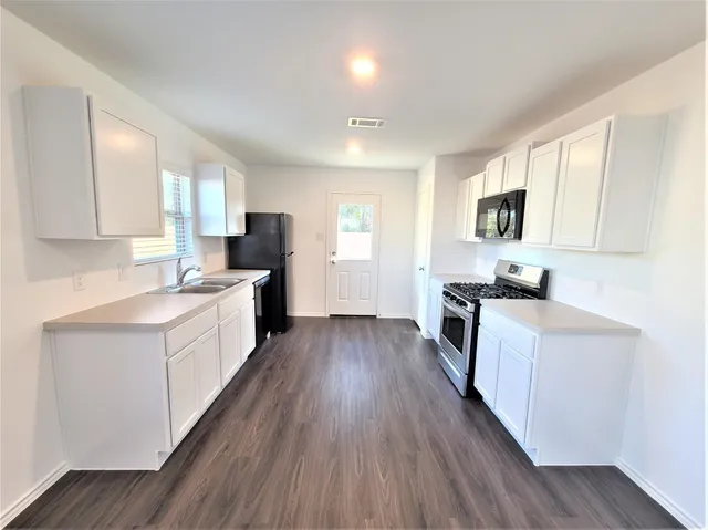 a large kitchen with a center island wooden floor stainless steel appliances and windows