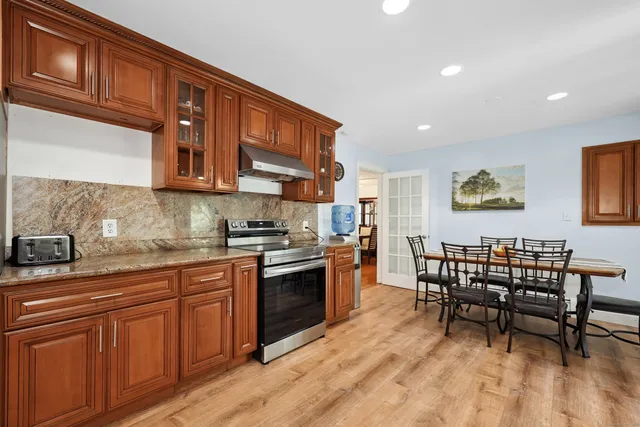 a kitchen with stainless steel appliances granite countertop a stove top oven a sink a dining table and chairs with wooden floor