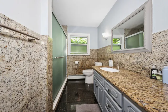 a bathroom with a granite countertop sink a toilet a mirror and shower