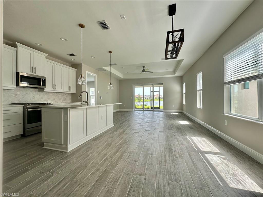 4580 Centaurus Circle Naples, FL 34120 - Photo 25 of 25 Kitchen featuring a raised ceiling, white cabinets, stainless steel appliances, hanging light fixtures, and open floor plan